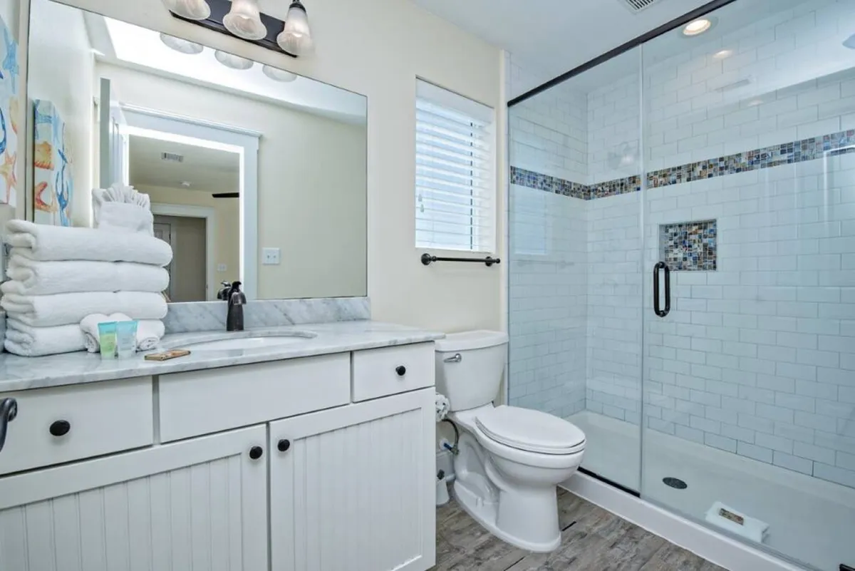 A spa-inspired bathroom with a mirrored vanity, neatly stacked towels, a glass shower enclosure, and a colorful shower curtain. The space feels serene and inviting, ideal for relaxation and personal grooming.