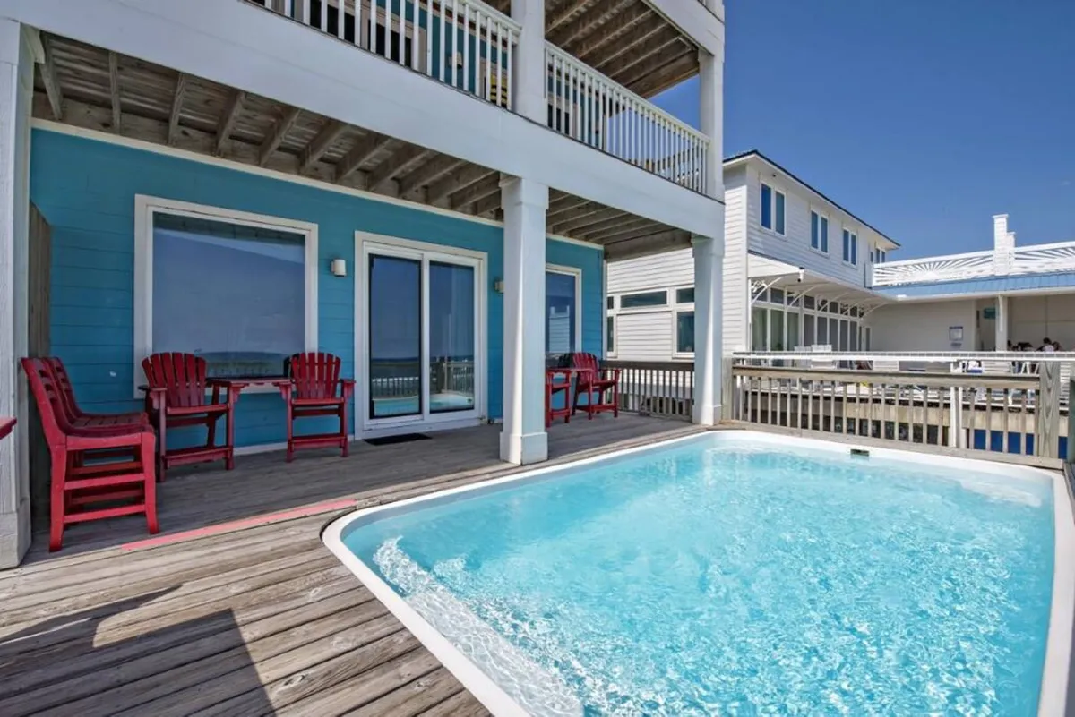 This exterior image presents a cheerful pool area with red chairs and a blue wall, set closely to the beach. The pool is inviting and appears ideal for post-beach fun, offering a relaxing spot for families to continue their day outdoors.