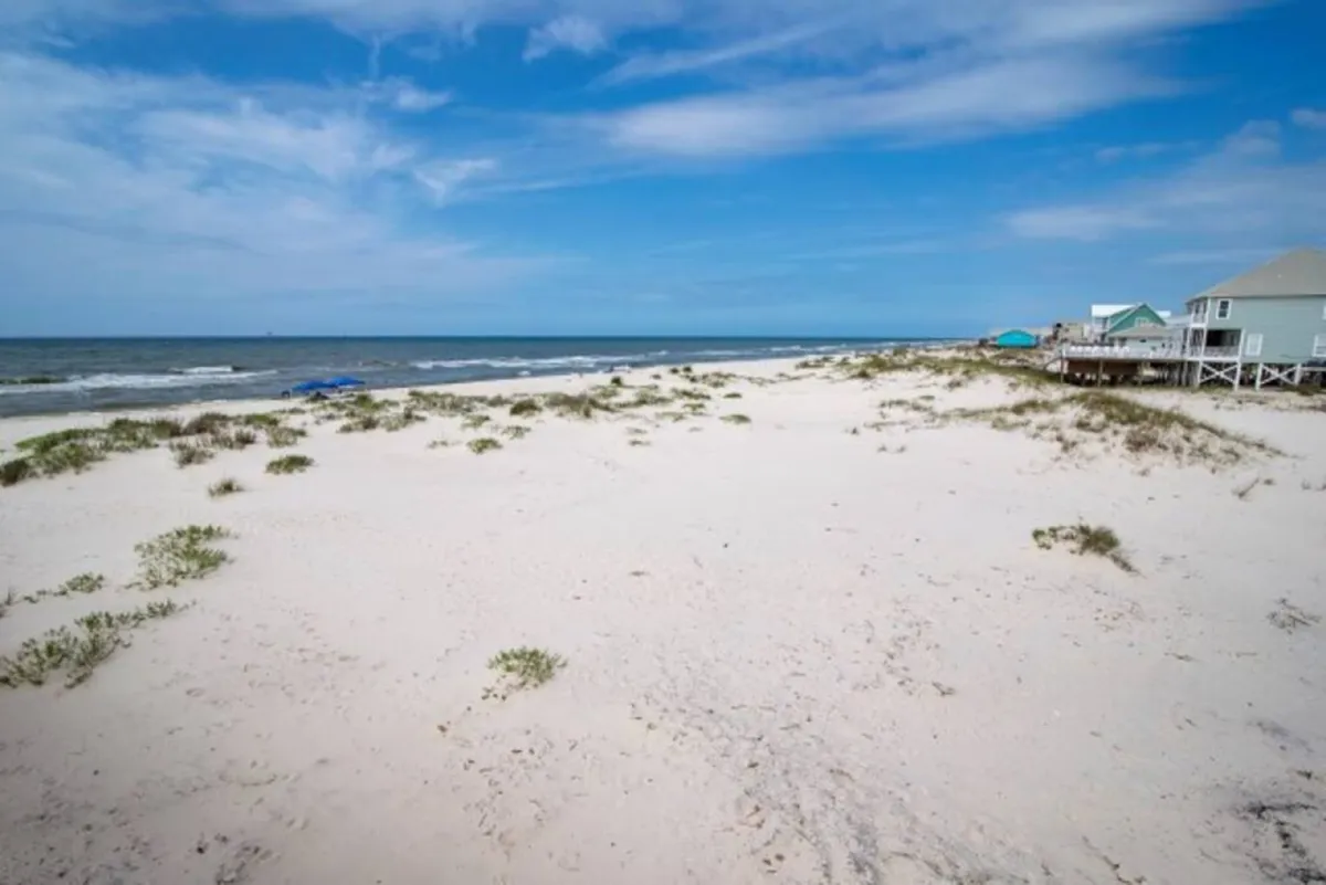 A wide, tranquil shot of an expansive sandy beach with calm ocean waves and distant beach houses. The open shoreline invites team-building activities such as sand volleyball or eco-tours, as described in the content.