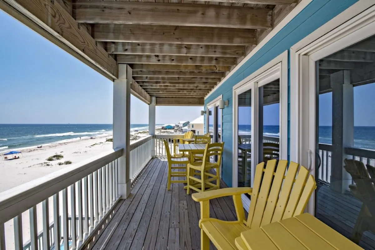 An inviting beachfront deck with yellow chairs, a clear ocean view, and a sturdy deck railing. The scene is relaxed and sociable, ideal for gatherings or simply soaking in the scenery.
