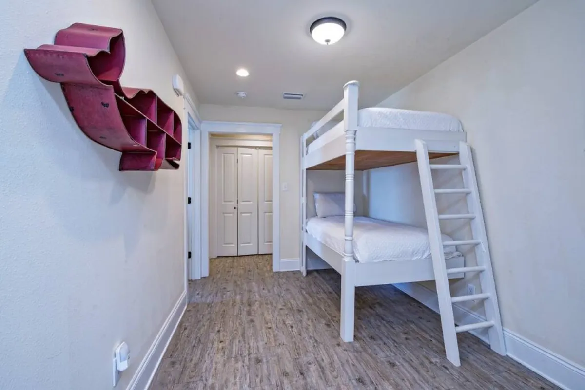 A bright, playful bunk room featuring a sturdy bunk bed, a red wall shelf for books or decor, and ample space for children to relax, read, or play. The atmosphere is both cozy and fun-filled, ideal for younger guests.