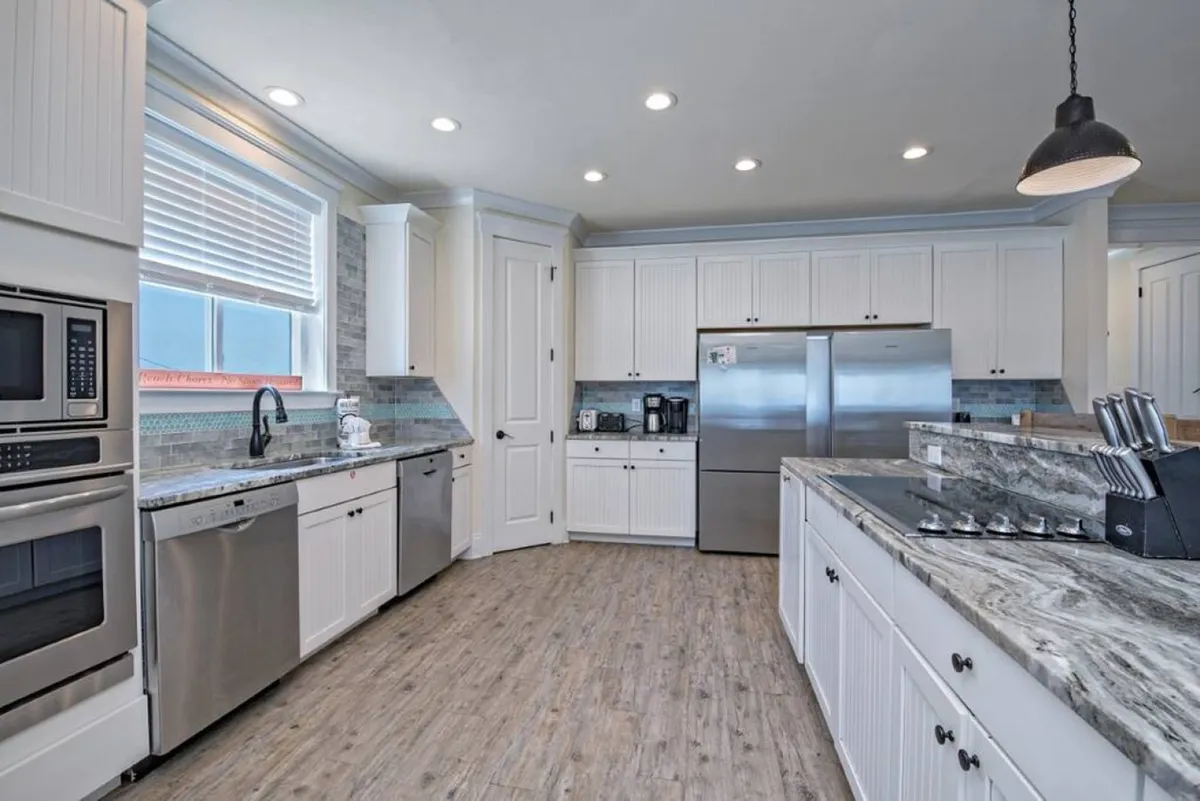 A modern kitchen with stainless steel appliances, granite countertops, white cabinetry, and a window bringing in natural light. The space is both stylish and functional, inviting culinary creativity and group meal preparation.
